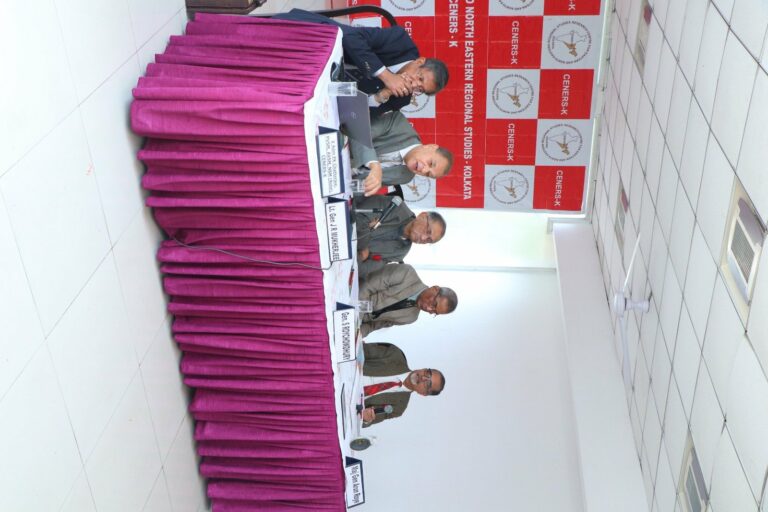 Overhead view of the CENERS-K panel table with magenta pleated skirting and name plates, panellists seated in front of the red CENERS-K banner wall.
