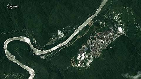 Satellite image of a developed town beside the braided channel of the Yarlung Tsangpo, ringed by dense forest.
